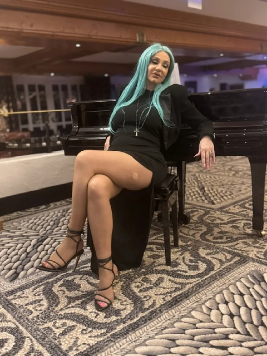 Michaela Hoppe vollständig in schwarzem Kleid mit feiner Strumpfhose und offenen Sandaletten an einem Flügel